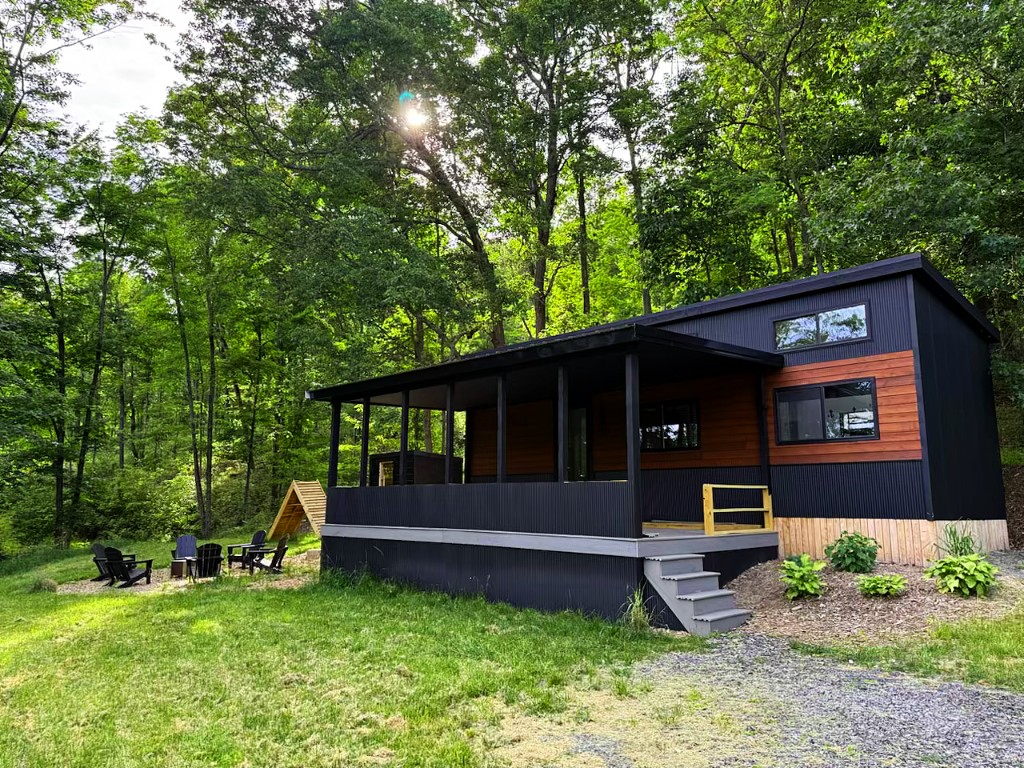 Anchor Twenty Eight cascade-style tiny home with black metal siding, wood accents, and covered porch in a wooded setting