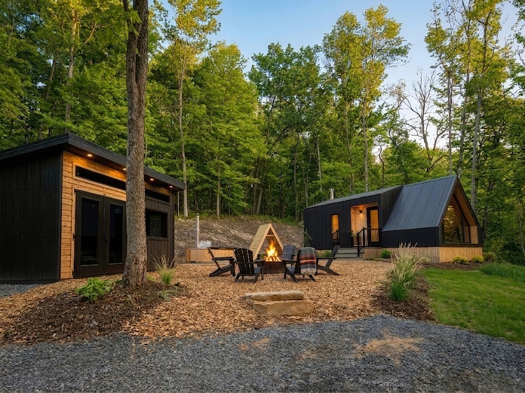 The Apex tiny home compound at dusk with fire pit, wood-fired hot tub, and sauna building among trees